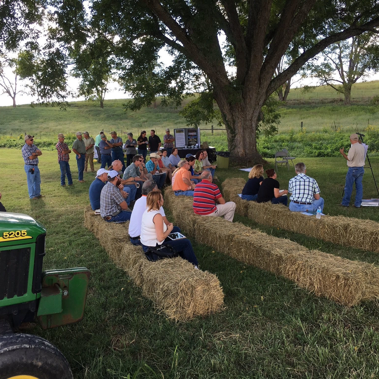 people sitting on hay bales in a field at an Extension field day 