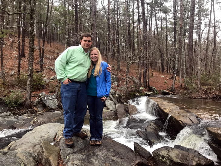 Sarah and her husband standing on rocks in the woods by a stream