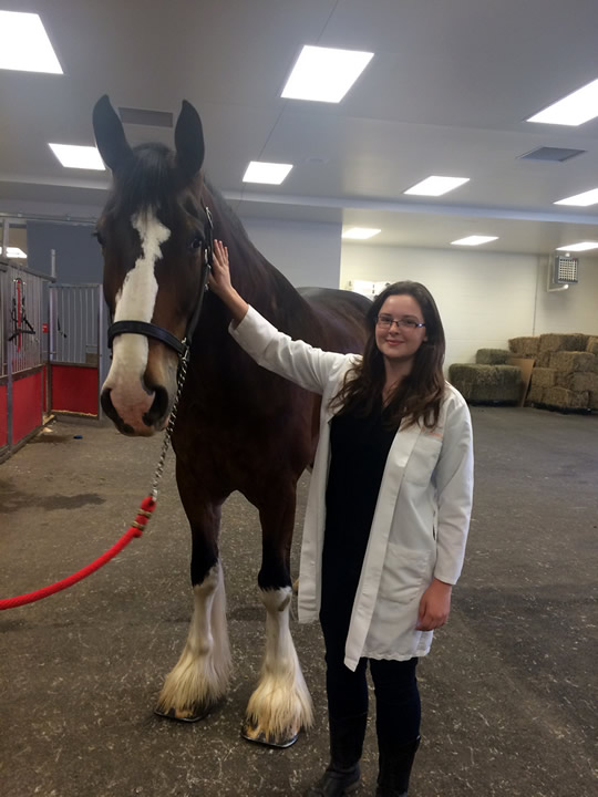 Kelly in a white coat petting a horse