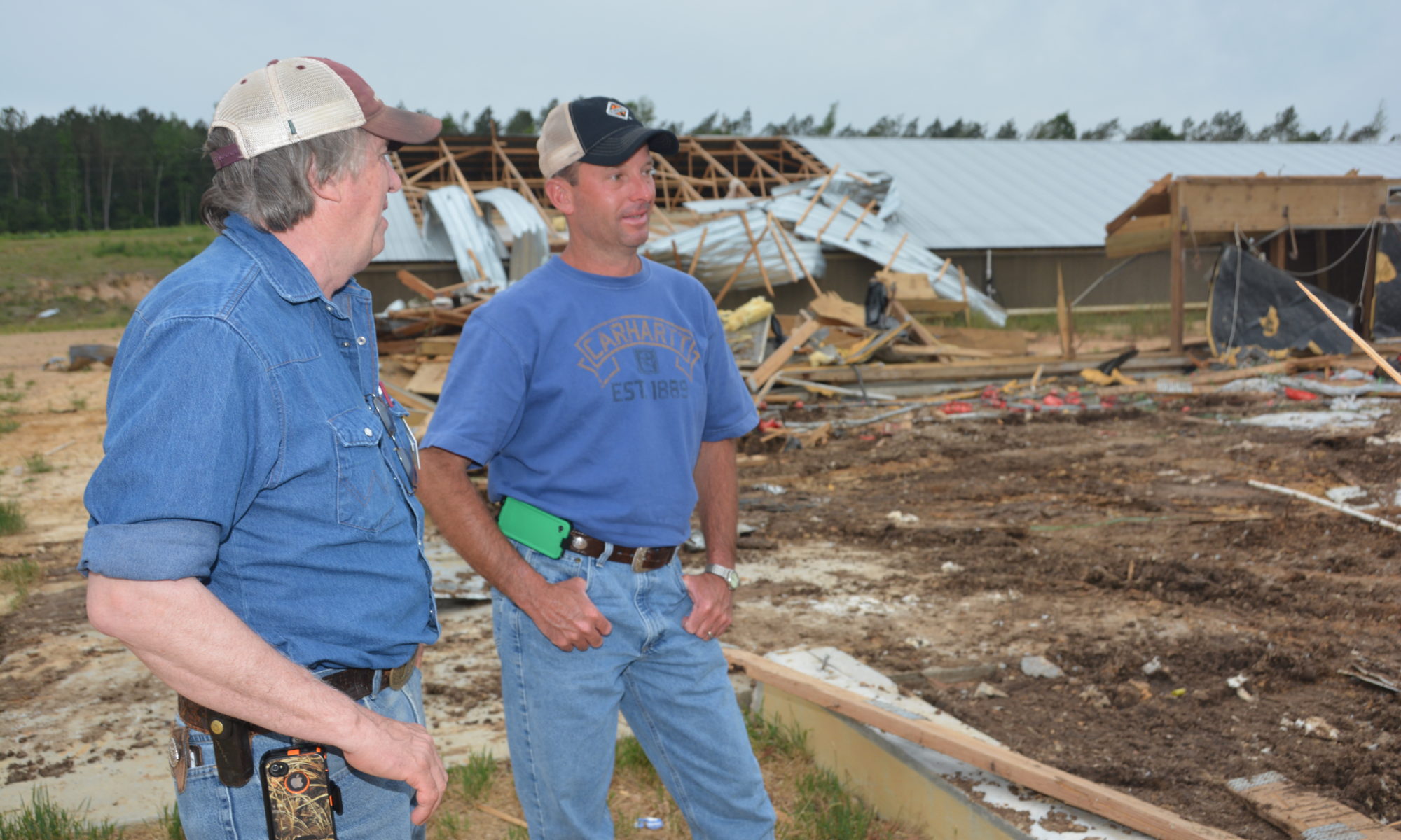 Tom Tabler standing in a field where a tornado has hit with a producer