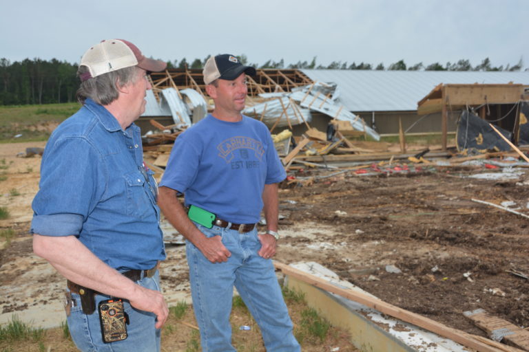 Tom Tabler standing in a field where a tornado has hit with a producer