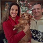 Sonia with her husband and dog standing in front of a Christmas tree