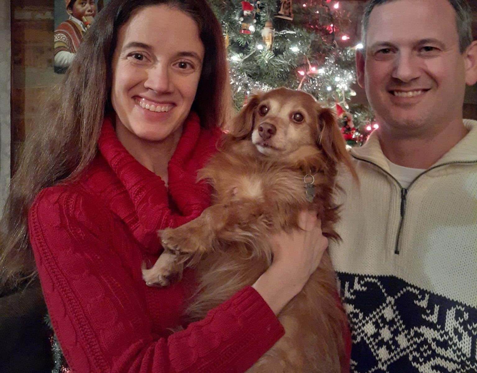 Sonia with her husband and dog standing in front of a Christmas tree