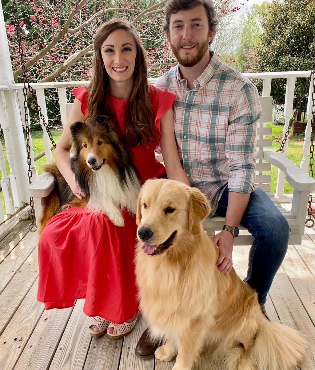 Taylor, her husband and two dogs sitting on a swing on a porch