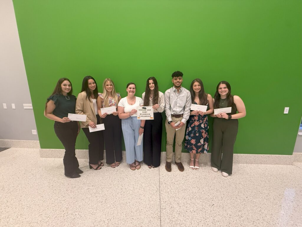 Students gathered together in front of a green wall for a picture
